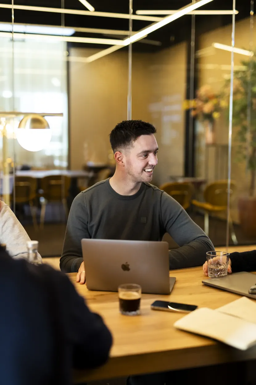 Collega werkt lachend op zijn laptop aan een vergadertafel
